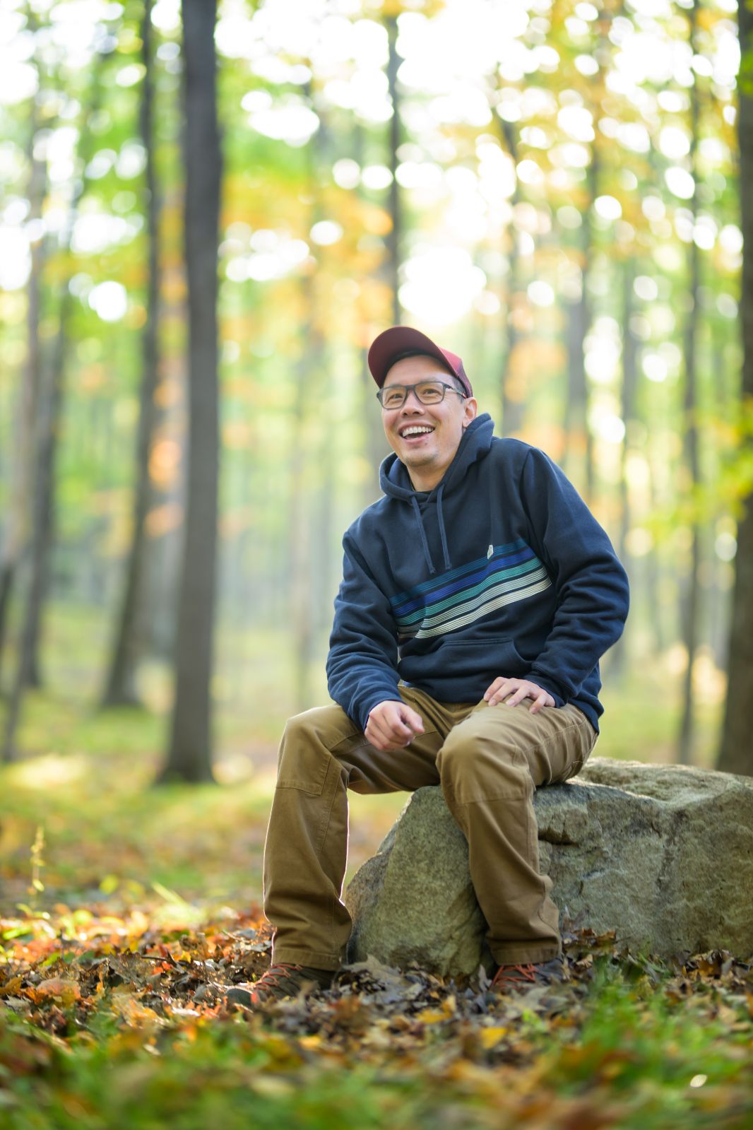 Sherman Cahal, sitting on a boulder in an autumn hardwood forest.